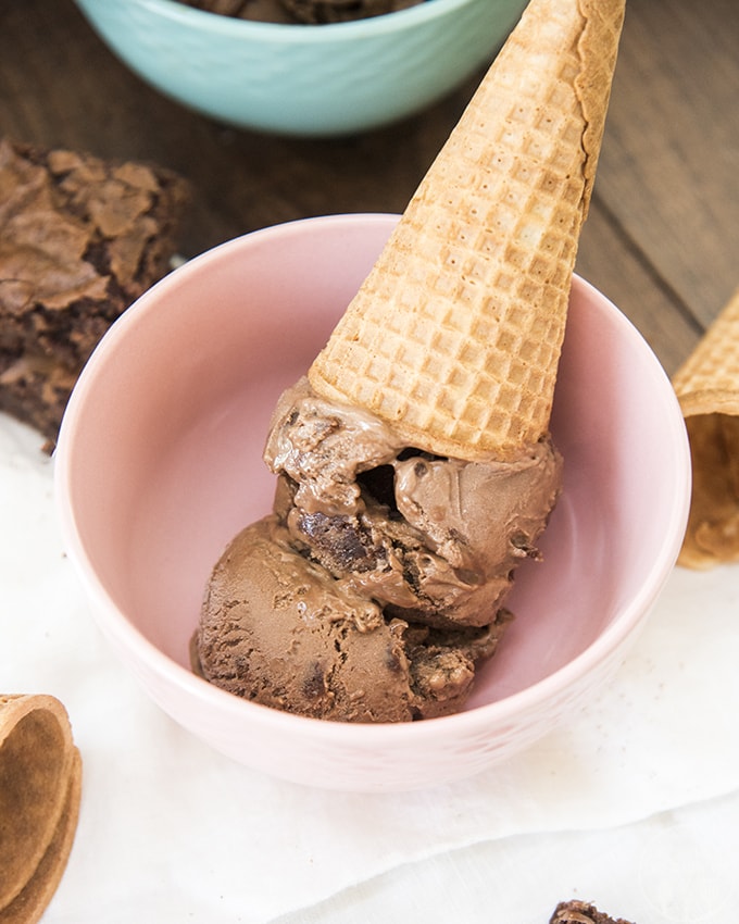 A chocolate brownie ice cream cone upside down in a pink bowl.