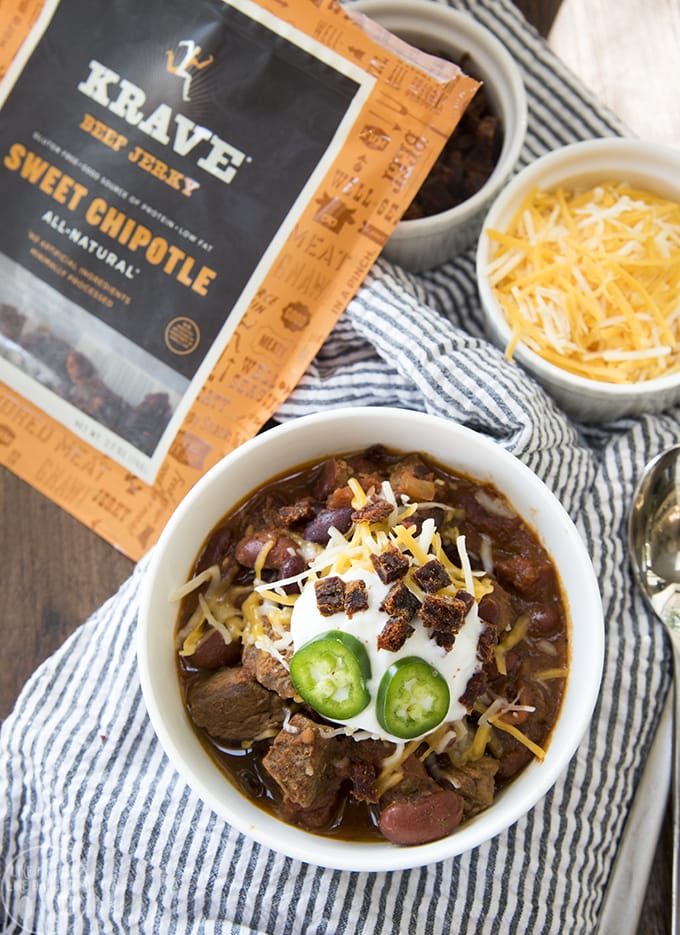 A bowl of steak chili next to a bag of beef jerky. 