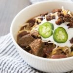 A bowl of steak chili topped with sour cream and jalapenos.
