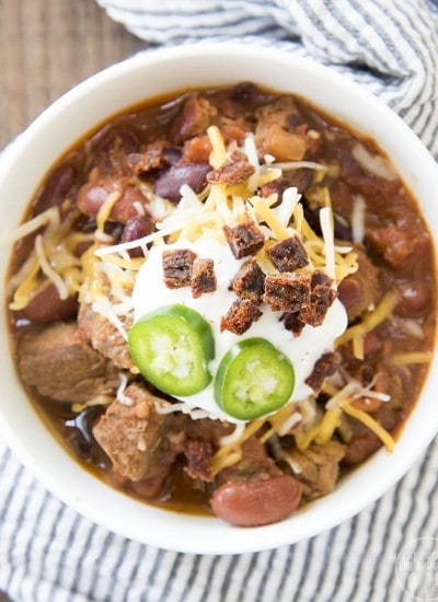 An overhead photo of a bowl of steak chili topped with sliced jalapenos, cheese, and jerky pieces.