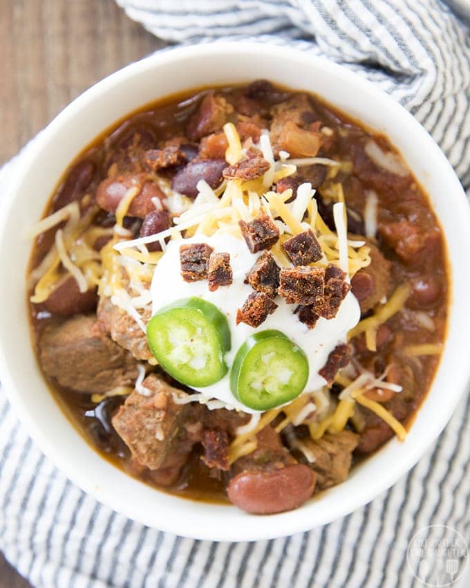 An overhead photo of a bowl of steak chili topped with sliced jalapenos, cheese, and jerky pieces. 
