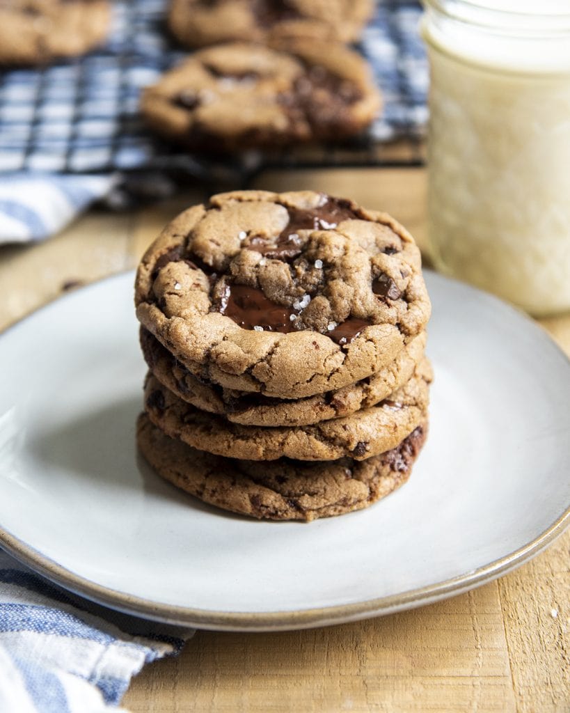A stack of Nutella chocolate chip cookies on a plate with a glass of milk behind it.