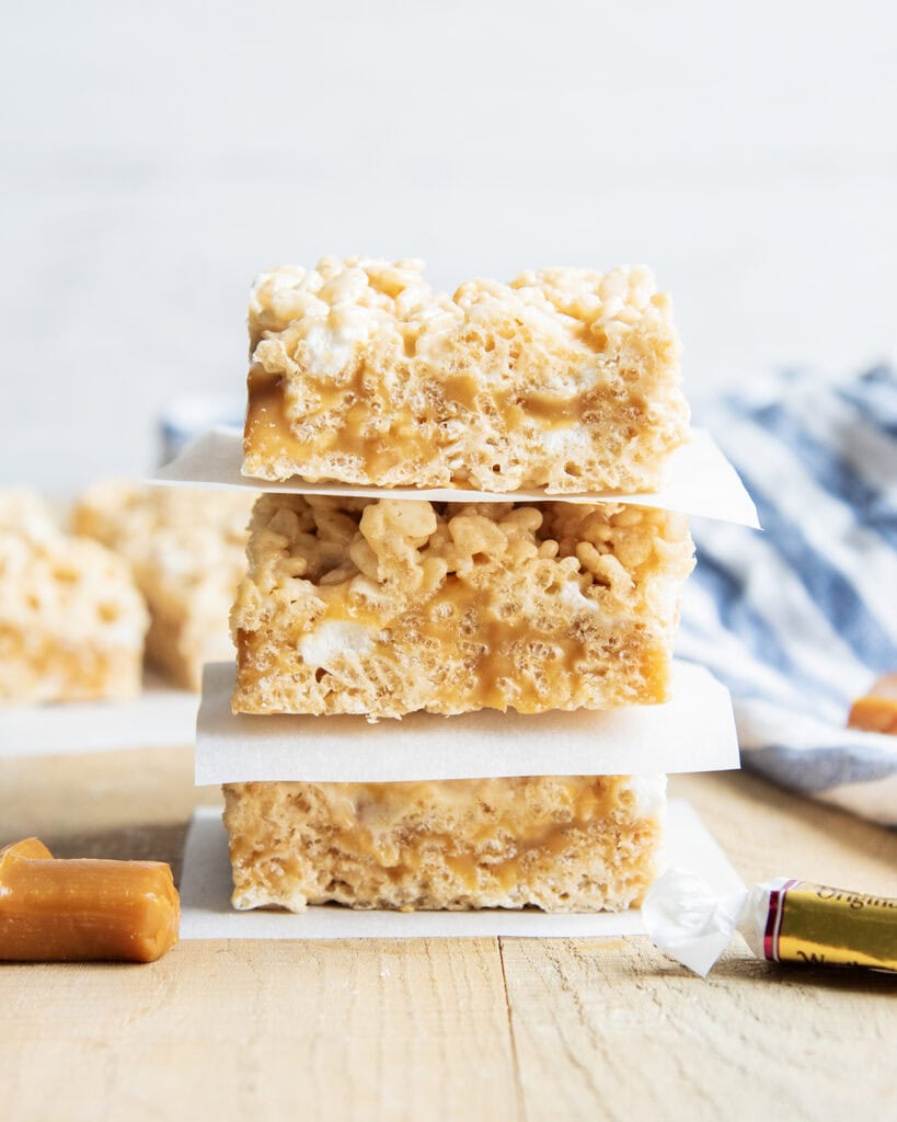 A stack of three caramel rice krispie treats, with pieces of parchment paper between them.