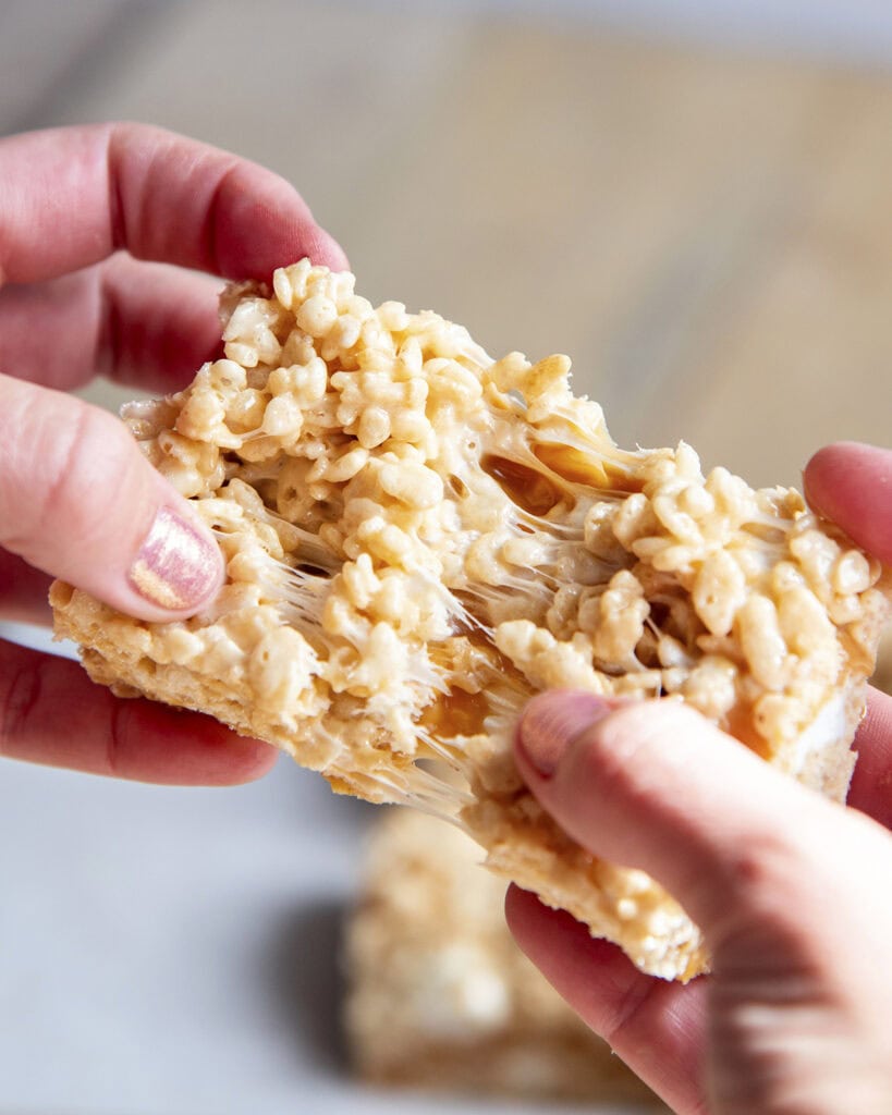 Two hands holding a rice krispie treat and pulling it apart, showing the gooey center.