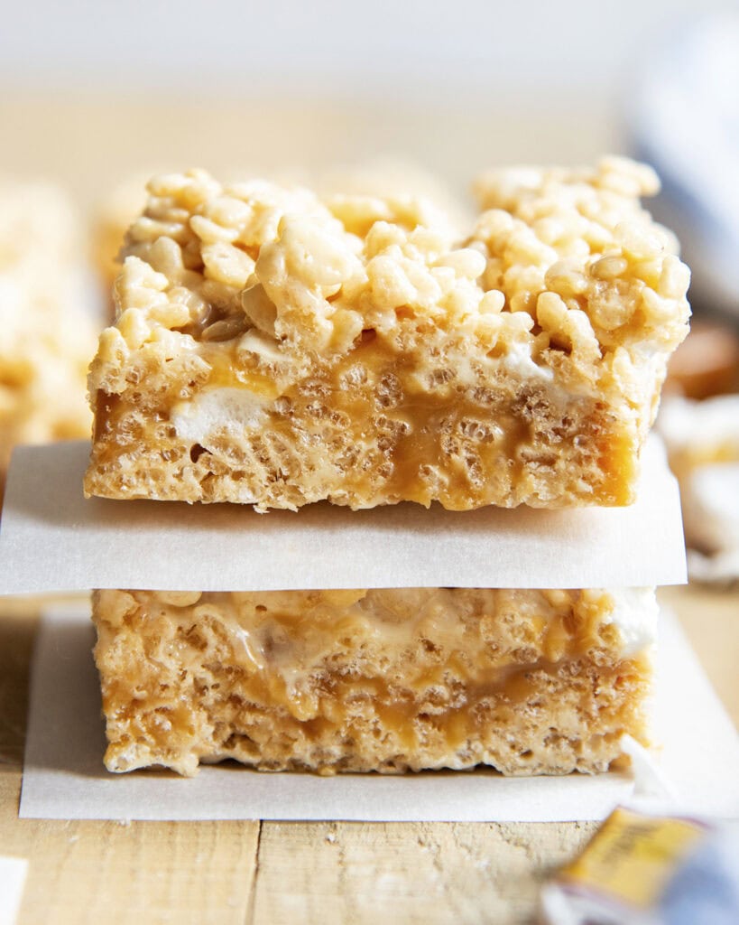 A stack of two caramel rice krispie treats, with a piece of parchment paper under each.