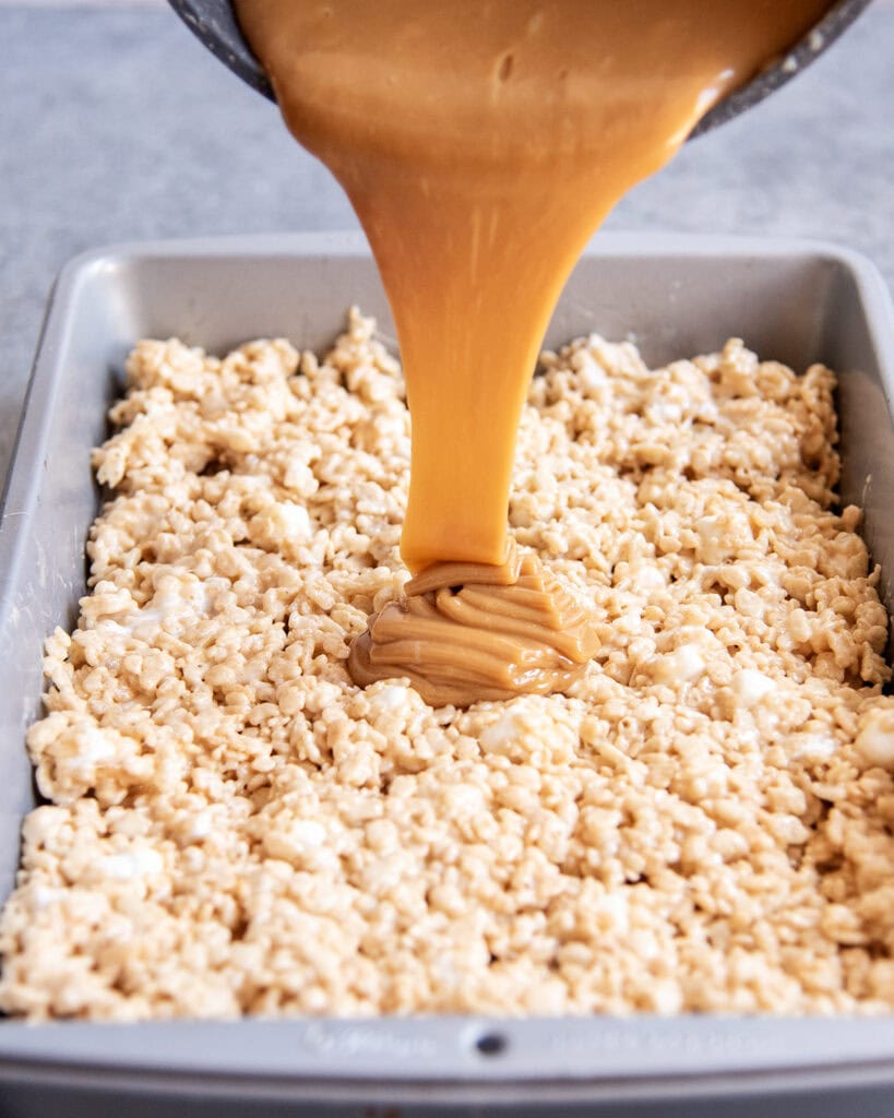 Caramel being poured out of a pan onto a tray of rice krispie treats.