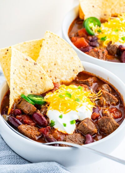 A bowl of steak chili topped with tortilla chips, sour cream, and cheddar cheese.