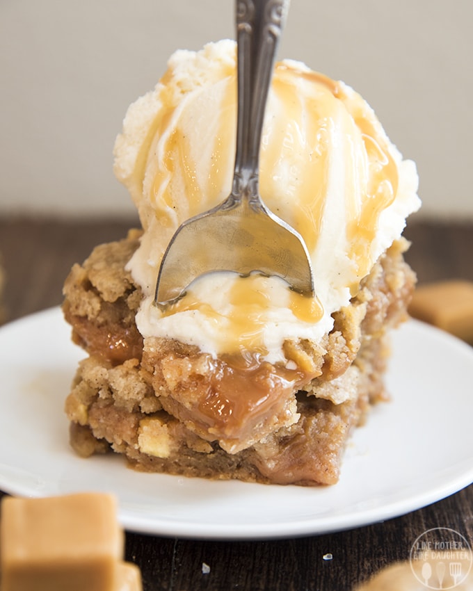Caramel apple blondies on a plate topped with vanilla ice cream and caramel syrup.