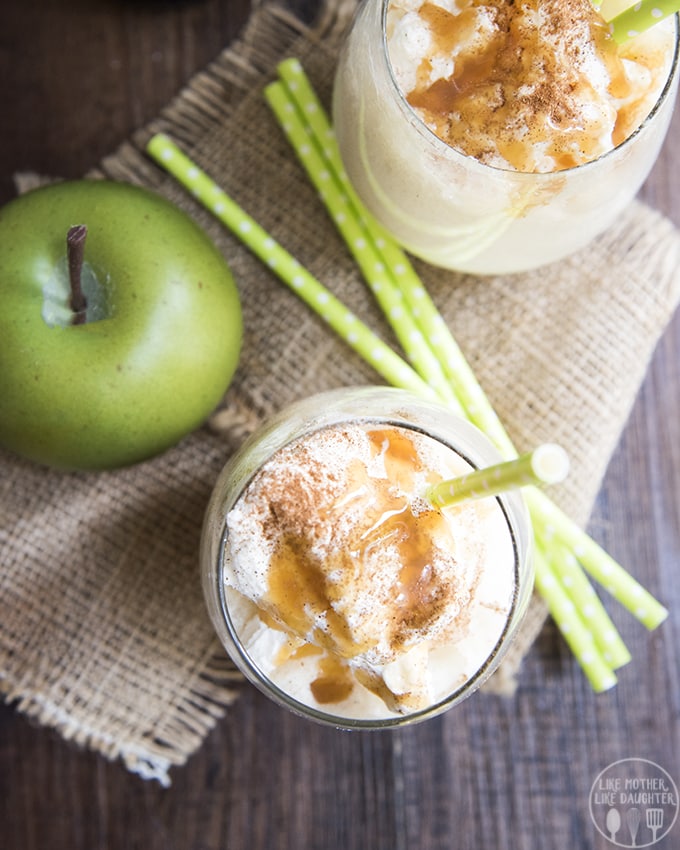 An overhead photo of a caramel apple cider drink in two glasses, and a green apple. 