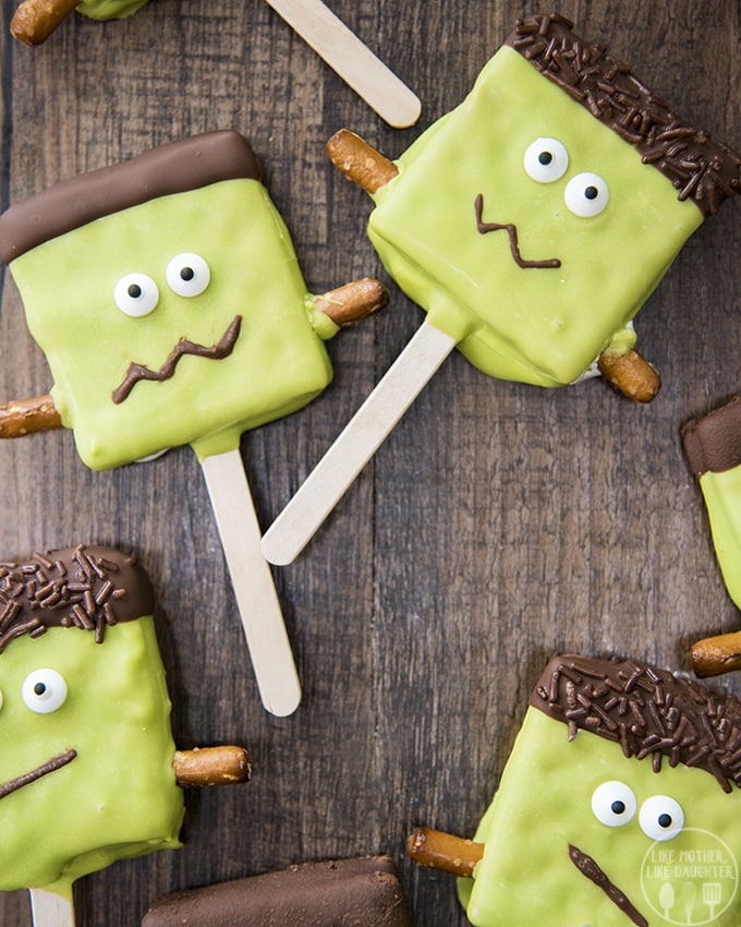 Frankenstein smores pops have marshmallow creme in the middle of two graham crackers and are dipped in chocolate to look just like Frankenstein.