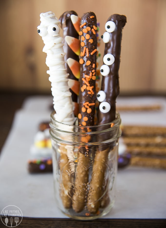 Long Halloween pretzels topped with orange sprinkles and candy eyes standing in a jar.