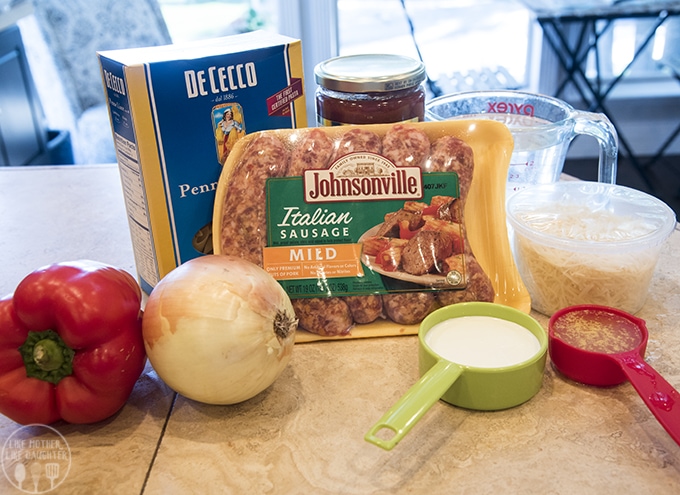 The ingredients needed to make one pot sausage pasta with sausages, penne pasta, bell pepper, onion, cream, and more. 