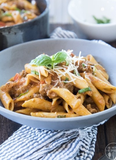 A bowl of penne pasta with sausage topped with shredded parmesan and fresh basil.