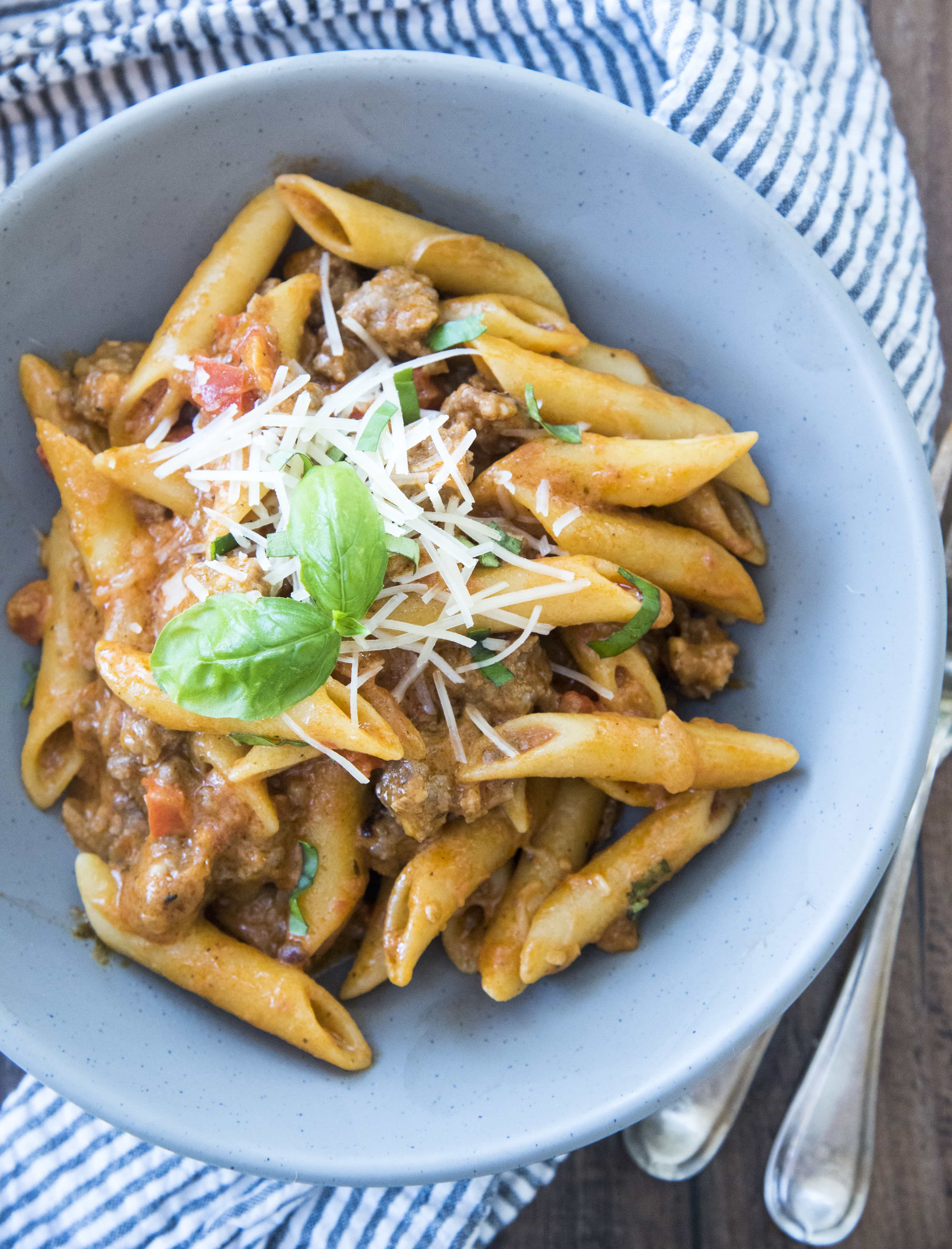 A grey bowl filled with penne pasta and sausage. 