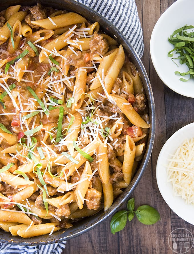 A pan of penne pasta covered in a creamy tomato sauce and sausage pieces. 