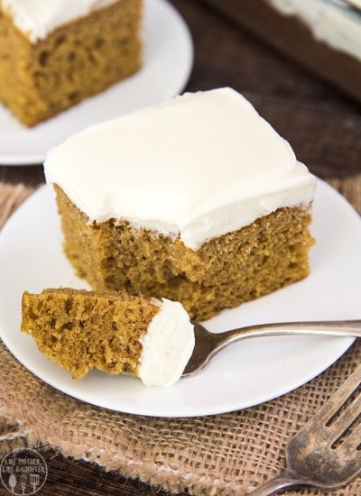 A square piece of pumpkin cake topped with a white cream cheese frosting with a  piece cut out on a fork.