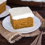 A square piece of pumpkin cake topped with cream cheese frosting on a plate.