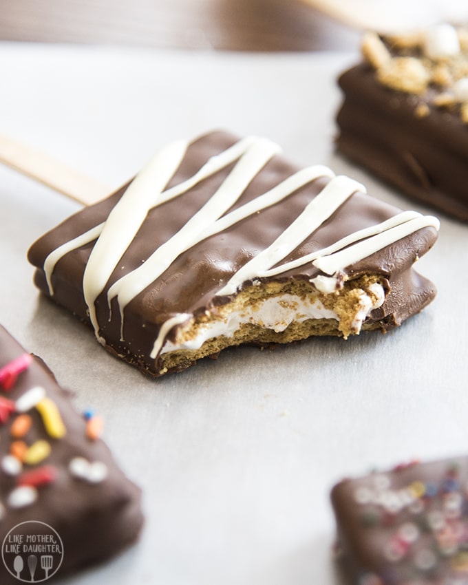 A smores pop with a bite out of it showing the graham cracker and marshmallow fluff in the middle. 