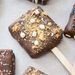 A chocolate covered smores pop on parchment paper.