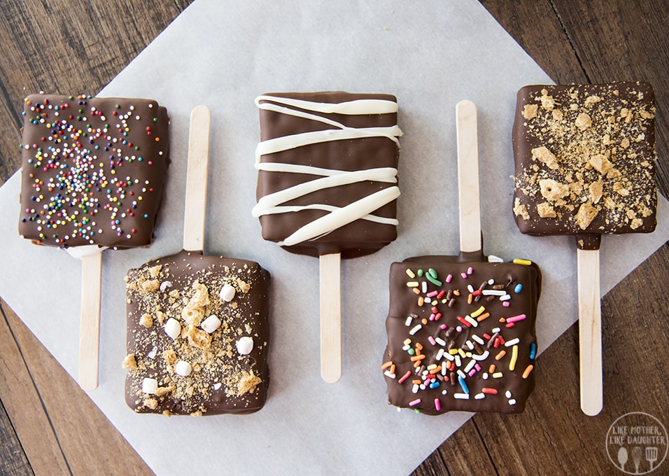 A row of 5 chocolate covered smores pops on popsicle sticks. 