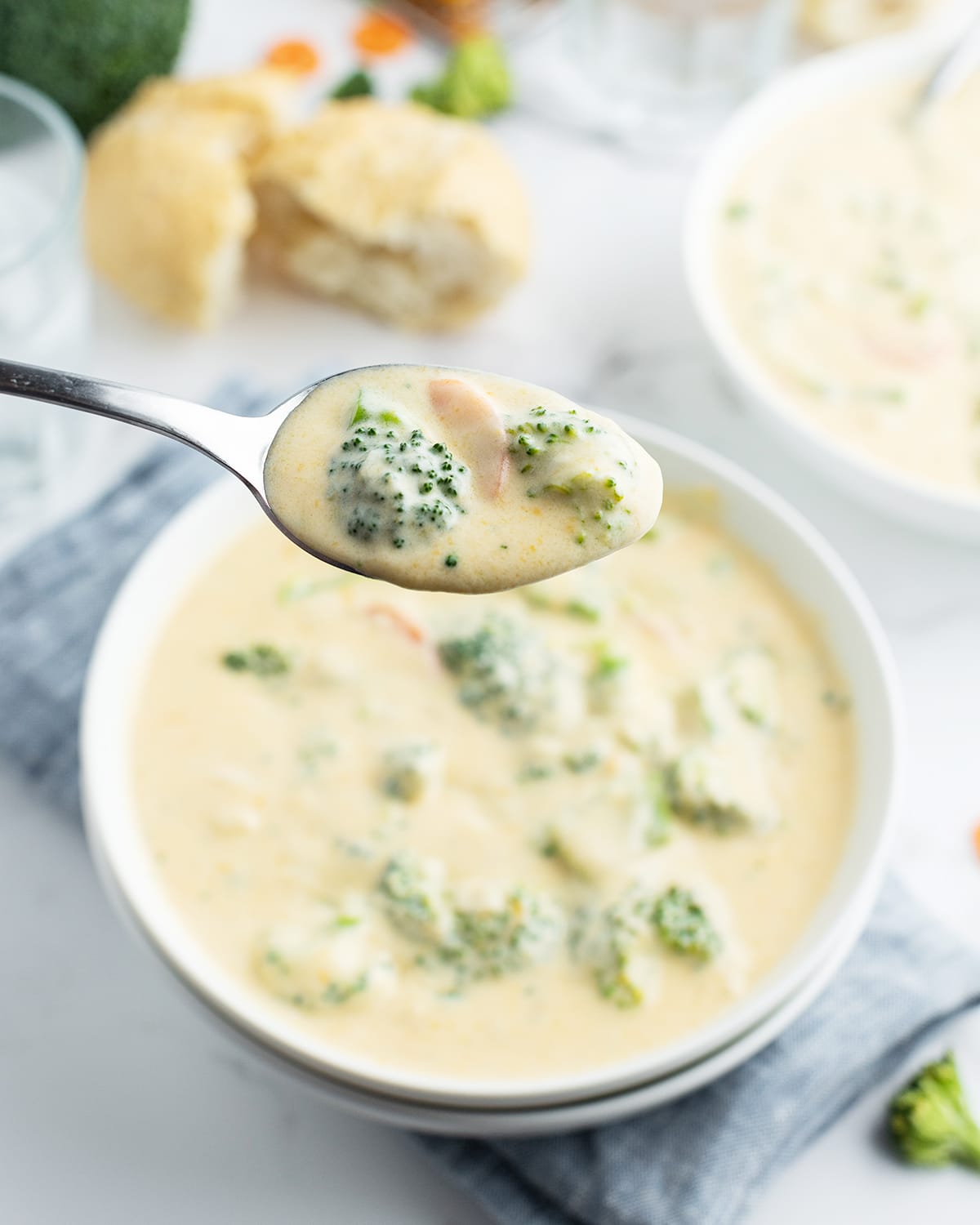 A spoonful of broccoli cheese soup above a bowl of broccoli cheese soup.