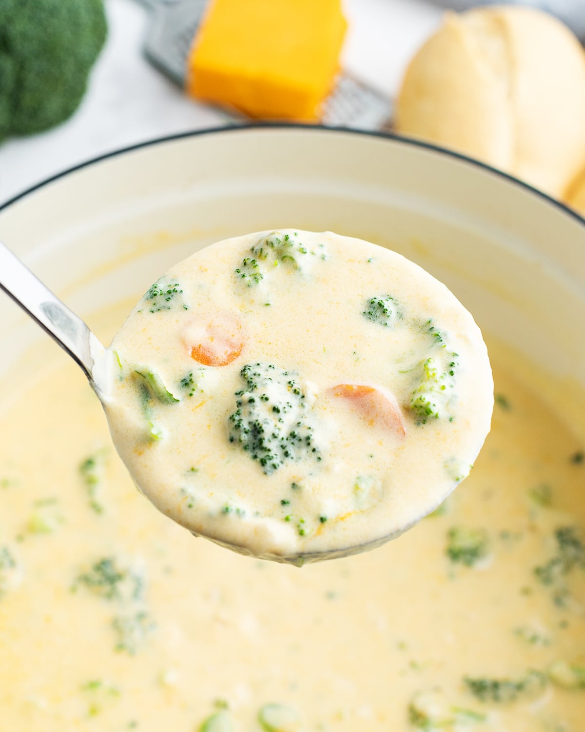 A ladle of broccoli cheese soup over a pot of the soup.