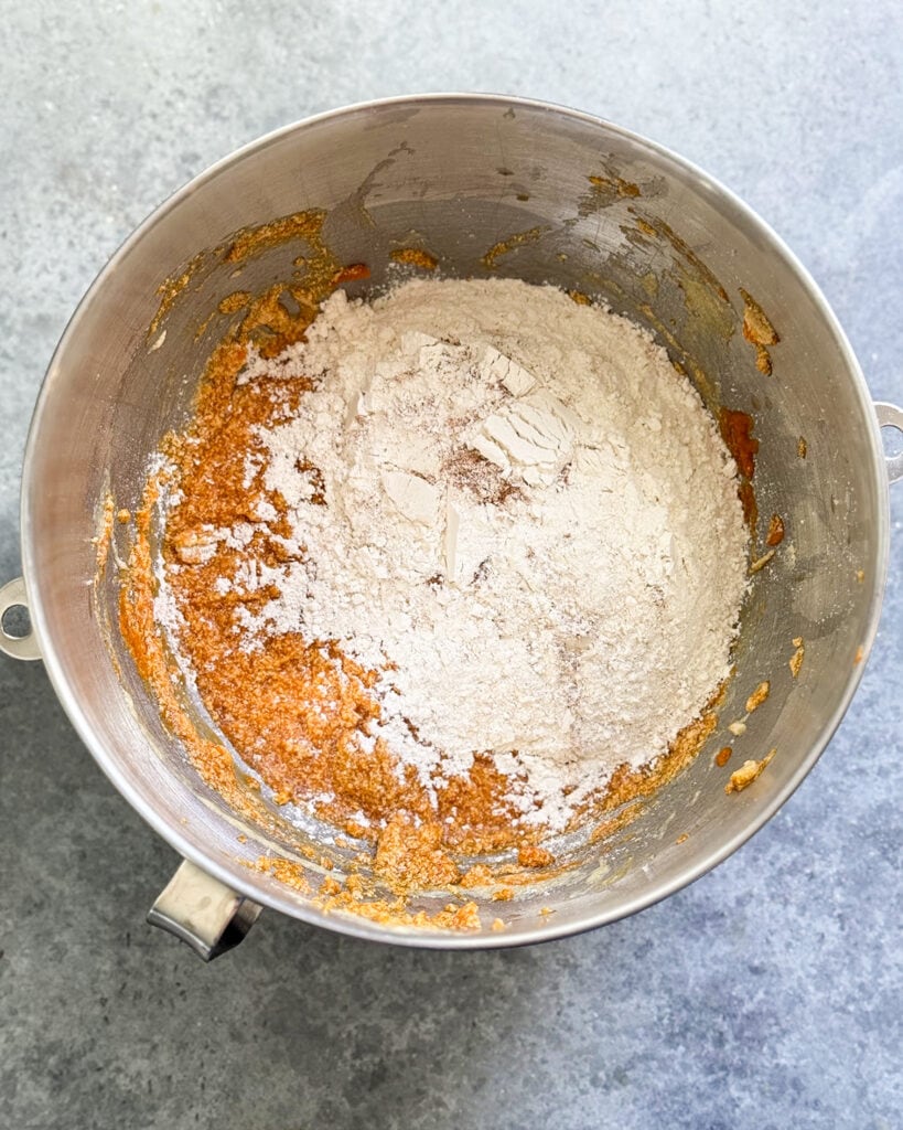 A bowl of a wet orange pumpkin mixture, topped with flour.