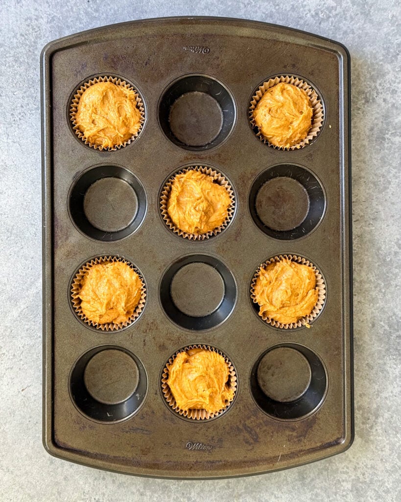 A muffin pan full of pumpkin muffin batter in every other muffin hole, leaving half empty.
