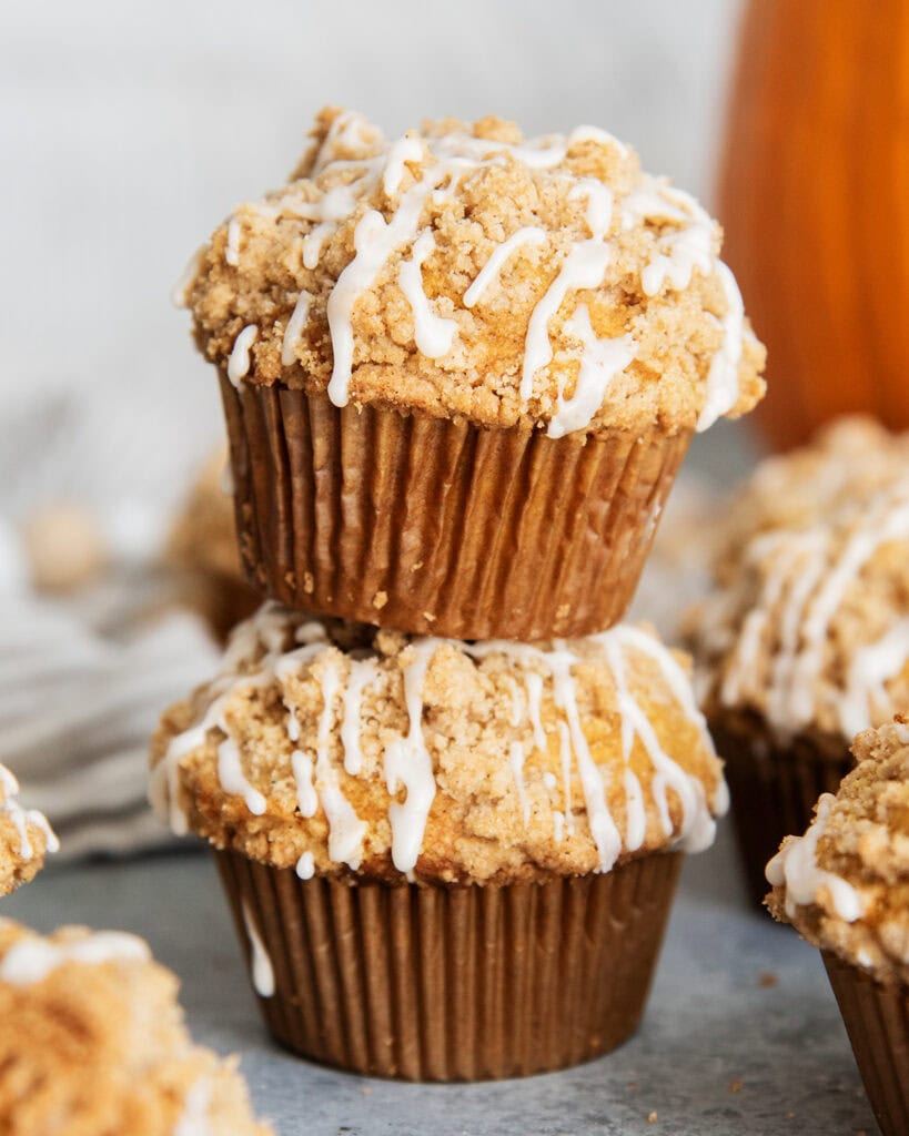 Two Pumpkin Muffins stacked on top of each other, each topped pile high with brown sugar crumb topping, and a white vanilla icing.