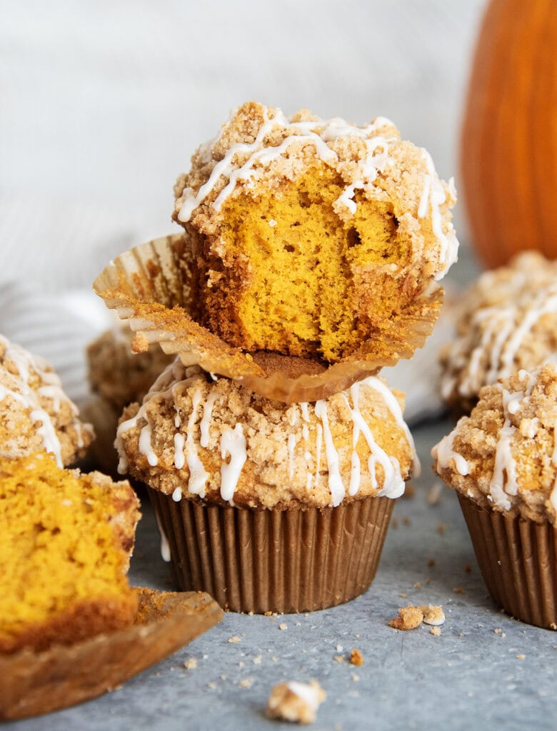 A pumpkin muffin with a bite out of it, on top of another high domed pumpkin muffin.