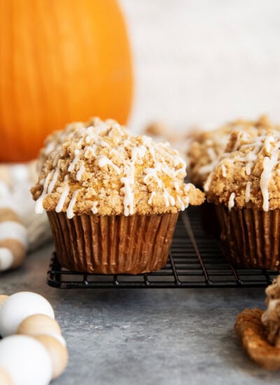 Tall Pumpkin Muffins topped with a streusel crumb and vanilla icing on a black cooling rack.