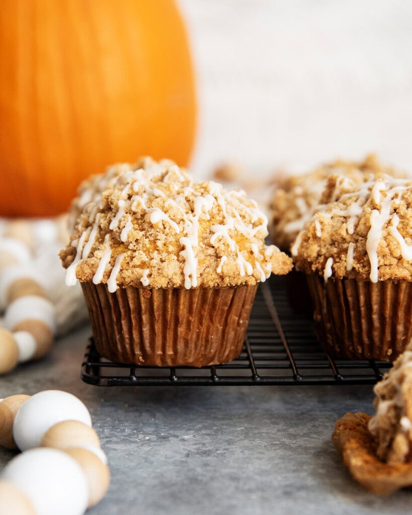 Tall Pumpkin Muffins topped with a streusel crumb and vanilla icing on a black cooling rack.