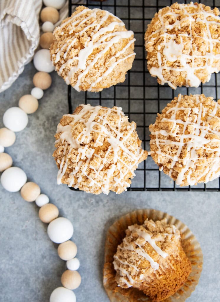 Tall Pumpkin Muffins topped with a streusel crumb and vanilla icing on a black cooling rack.