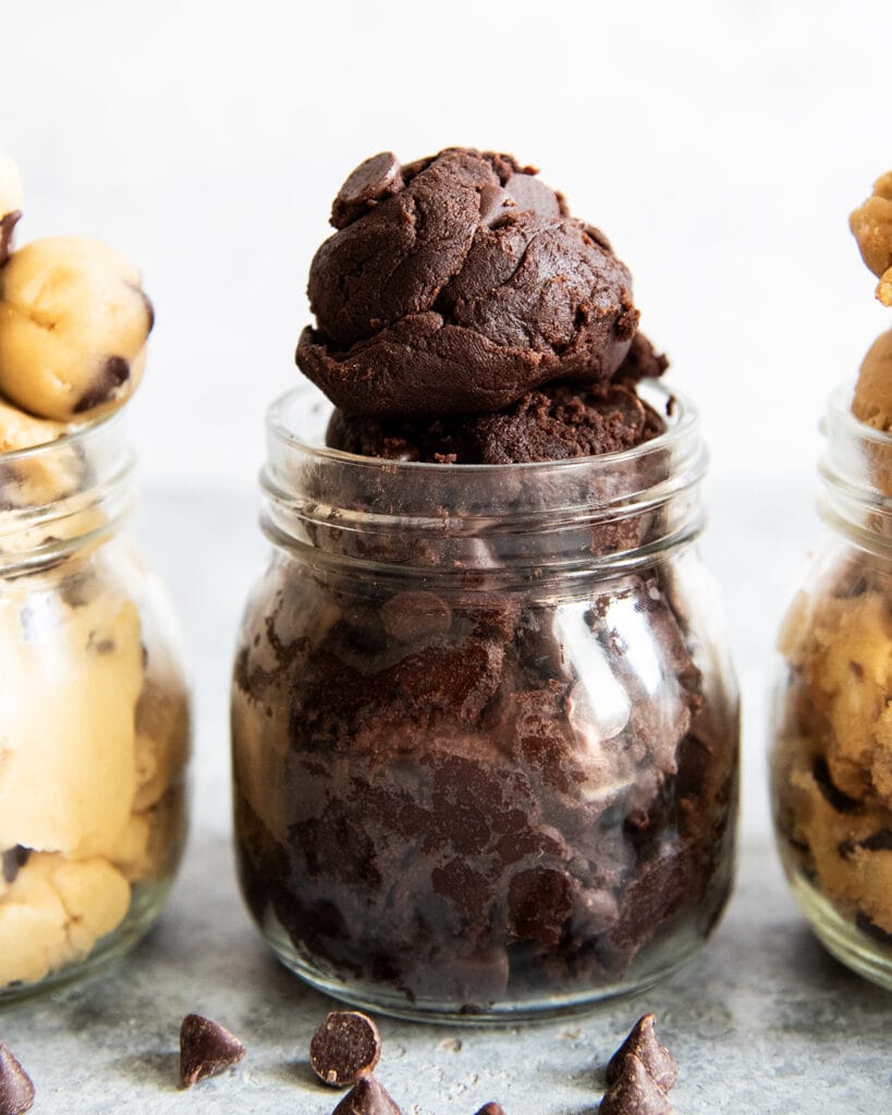 A glass jar full of double chocolate cookie dough with a big scoop of cookie dough coming out the top of the jar.