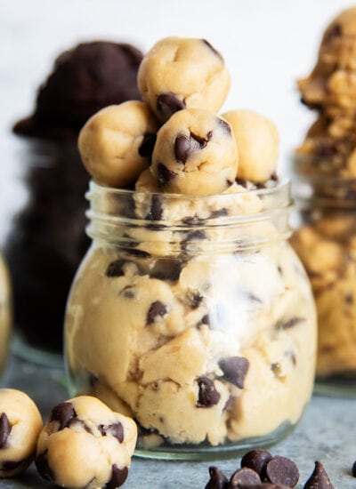 A jar of edible chocolate chip cookie dough topped with small balls of cookie dough, and with small balls in front of the jar too.