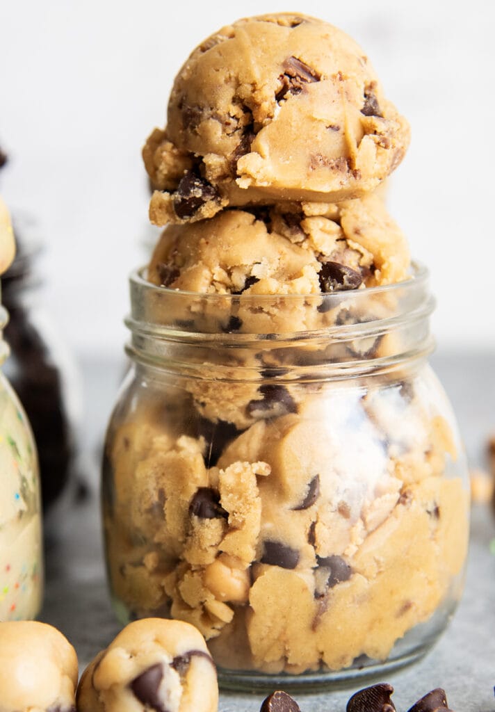 A glass jar of peanut butter cookie dough, with two big scoops of cookie dough coming out of the top of the jar. 