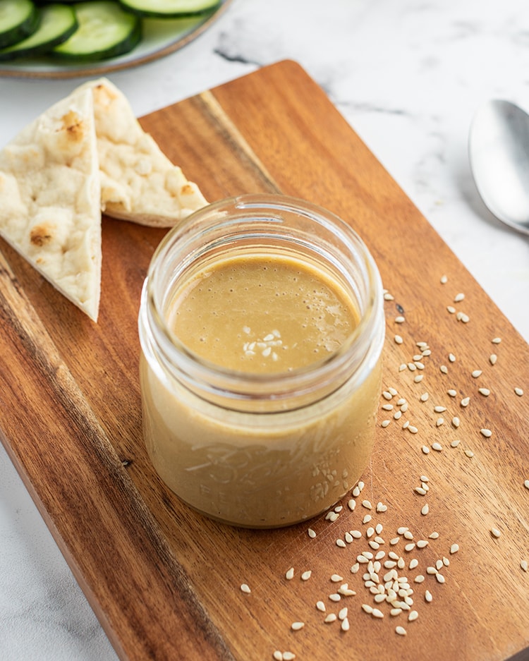 A small jar of tahini on a wooden board.