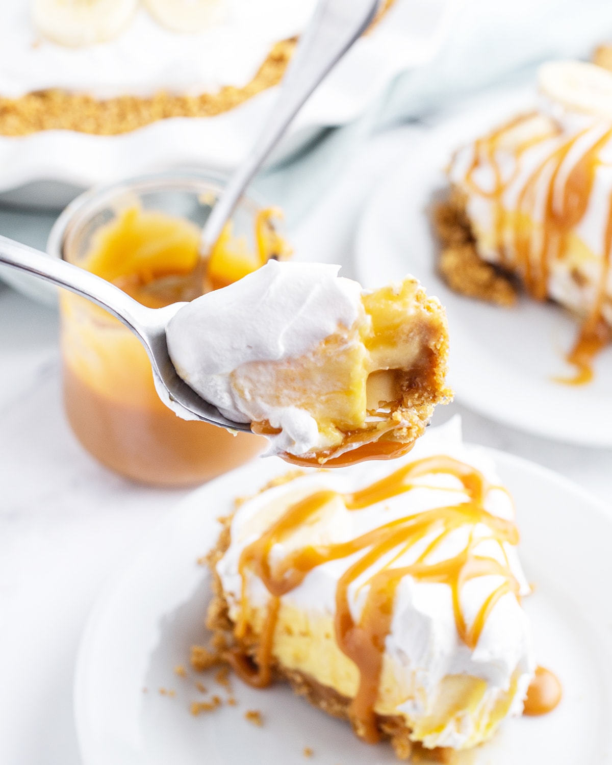 A bite of caramel banana cream pie being held about a slice of the pie.