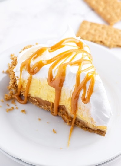A slice of caramel banana cream pie on a white plate topped with caramel sauce.