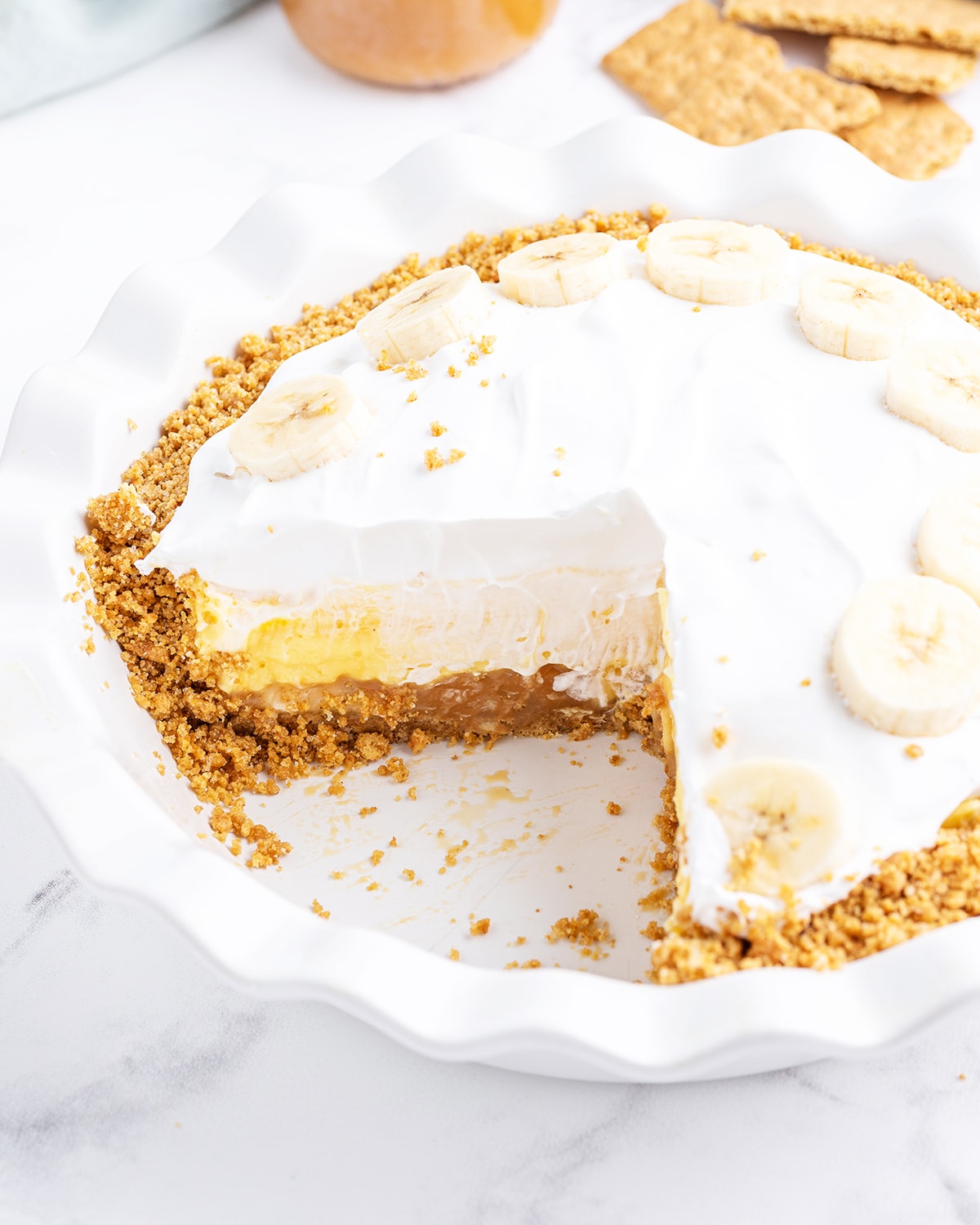 A caramel banana cream pie that is cut into in the pie plate.