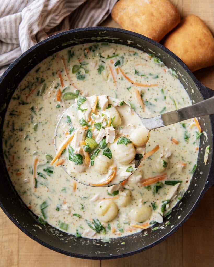 A pot of soup with a white creamy base, potato gnocchi and chicken.