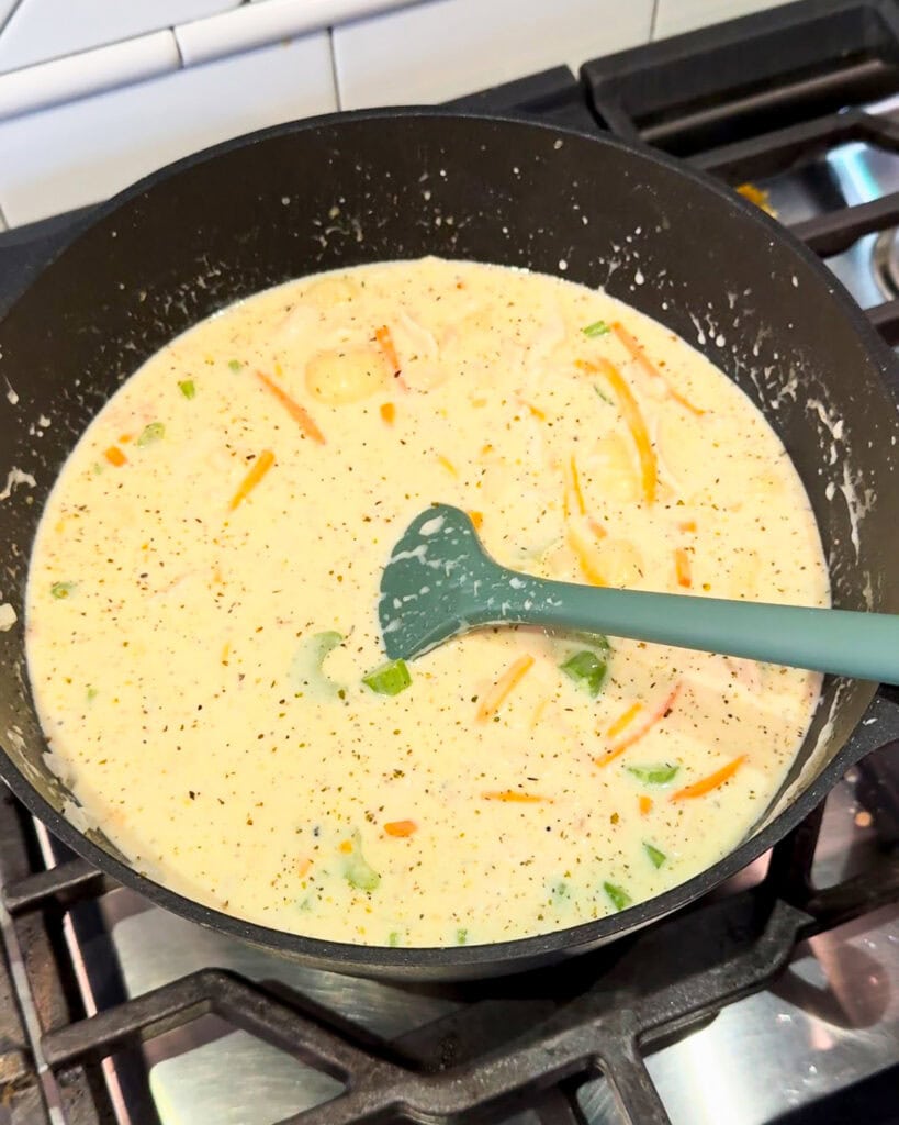 A pot  of creamy soup with carrots and gnocchi.