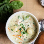 An above view of two bowls of creamy gnocchi soup with chicken, carrots, and celery.