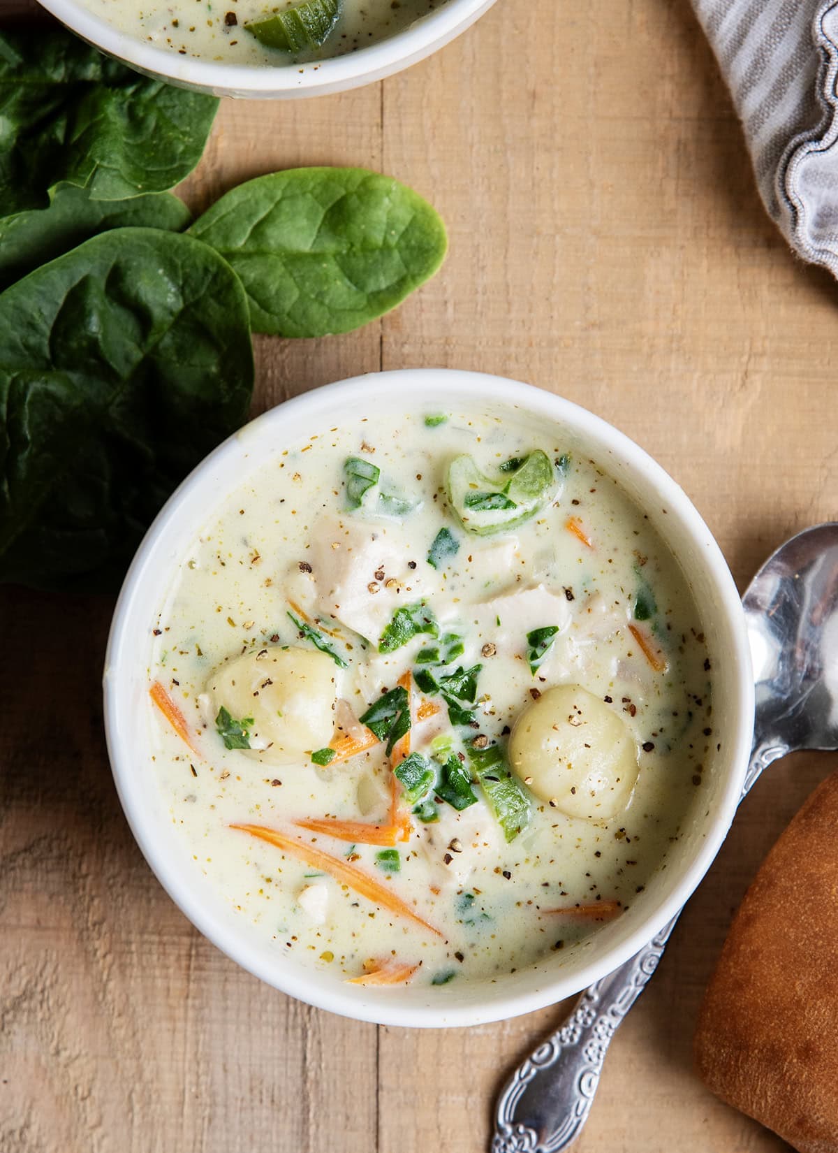 An above view of two bowls of creamy gnocchi soup with chicken, carrots, and celery.