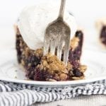A piece of blueberry pie with a crumble on top, and a fork taking a bite out of the front.