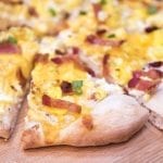A slice of breakfast pie topped with cheese, bacon, and green onion.