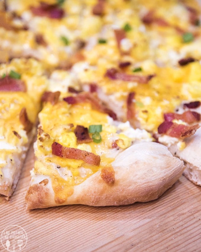 A slice of breakfast pie topped with cheese, bacon, and green onion.