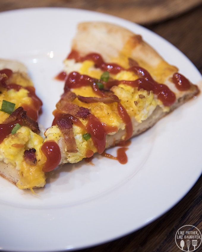 A slice of breakfast pizza on a plate topped with ketchup.
