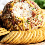 A bacon and cheddar cheese covered cheese ball with some of the outside taken out to show the center.