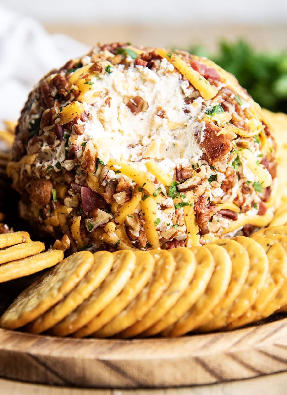 A bacon and cheddar cheese covered cheese ball with some of the outside taken out to show the center.